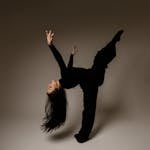 A dancer in a dynamic black outfit performing an elegant contemporary pose.