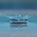 Macro shot of a water droplet creating a ripple effect on the water surface.