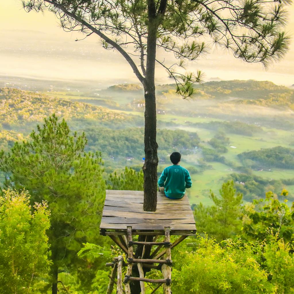 A person enjoying a tranquil moment on a wooden platform amidst lush, misty forests in Indonesia.