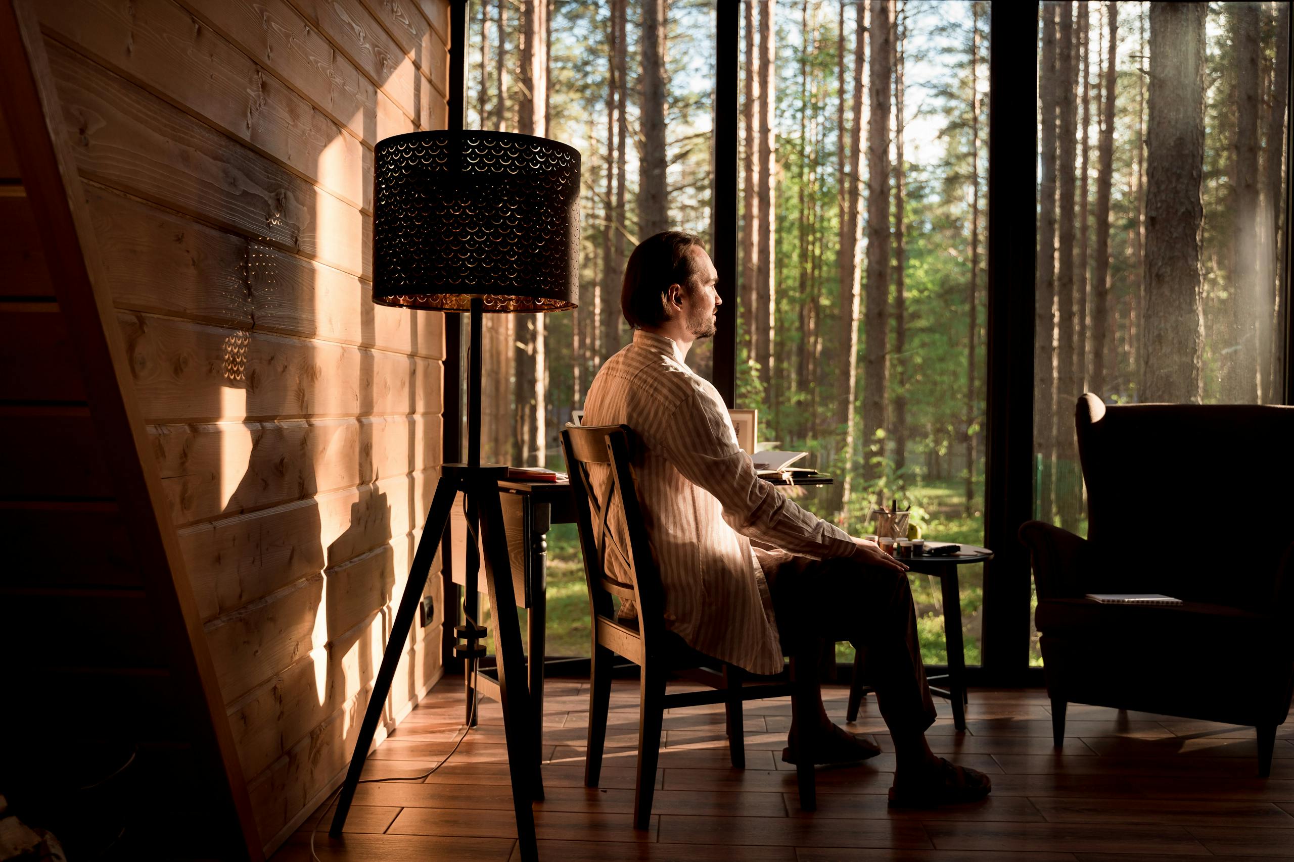 A man sitting in a serene forest cabin interior, enjoying the tranquil view outside.