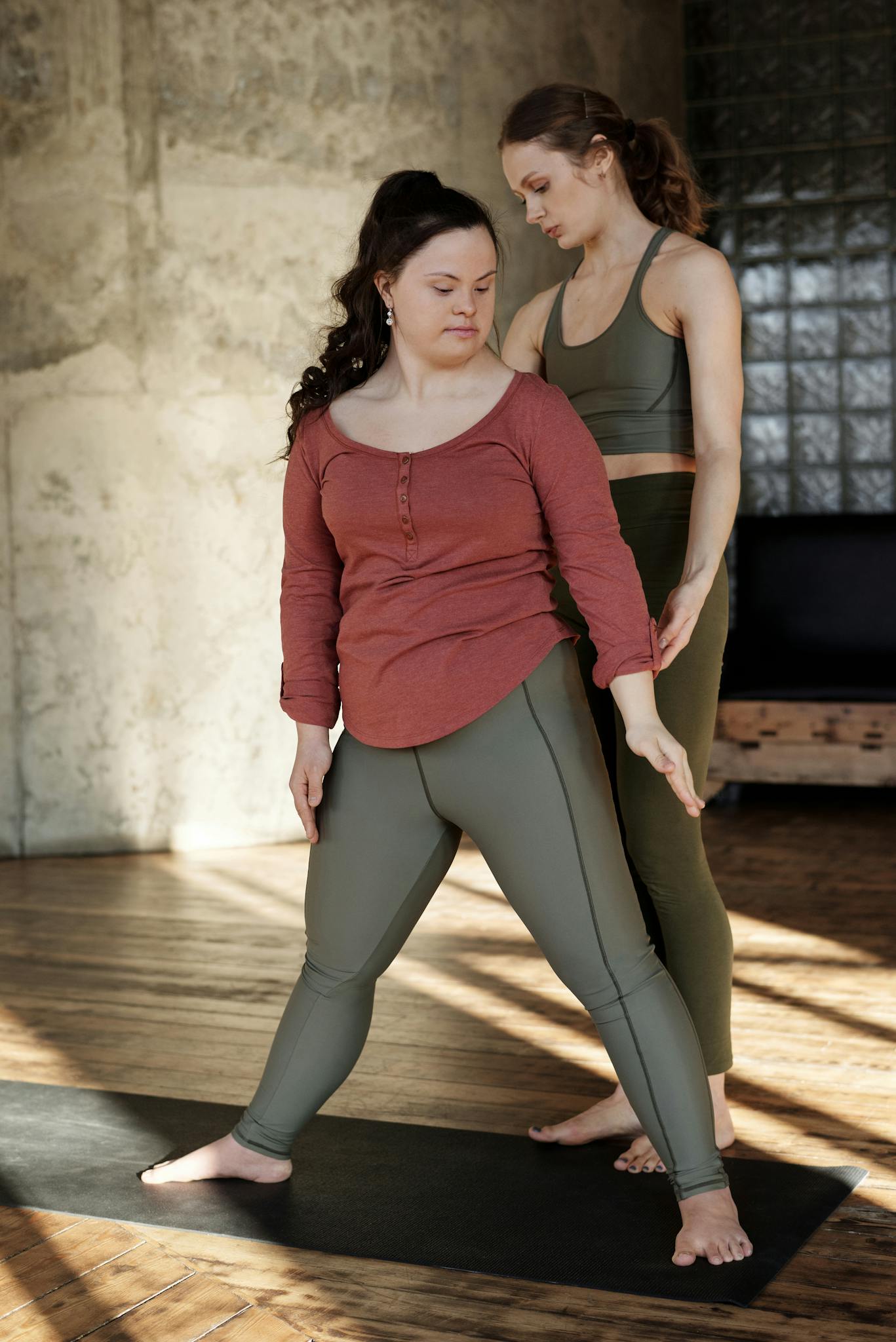 A woman with Down syndrome practices yoga with guidance from a personal trainer indoors.
